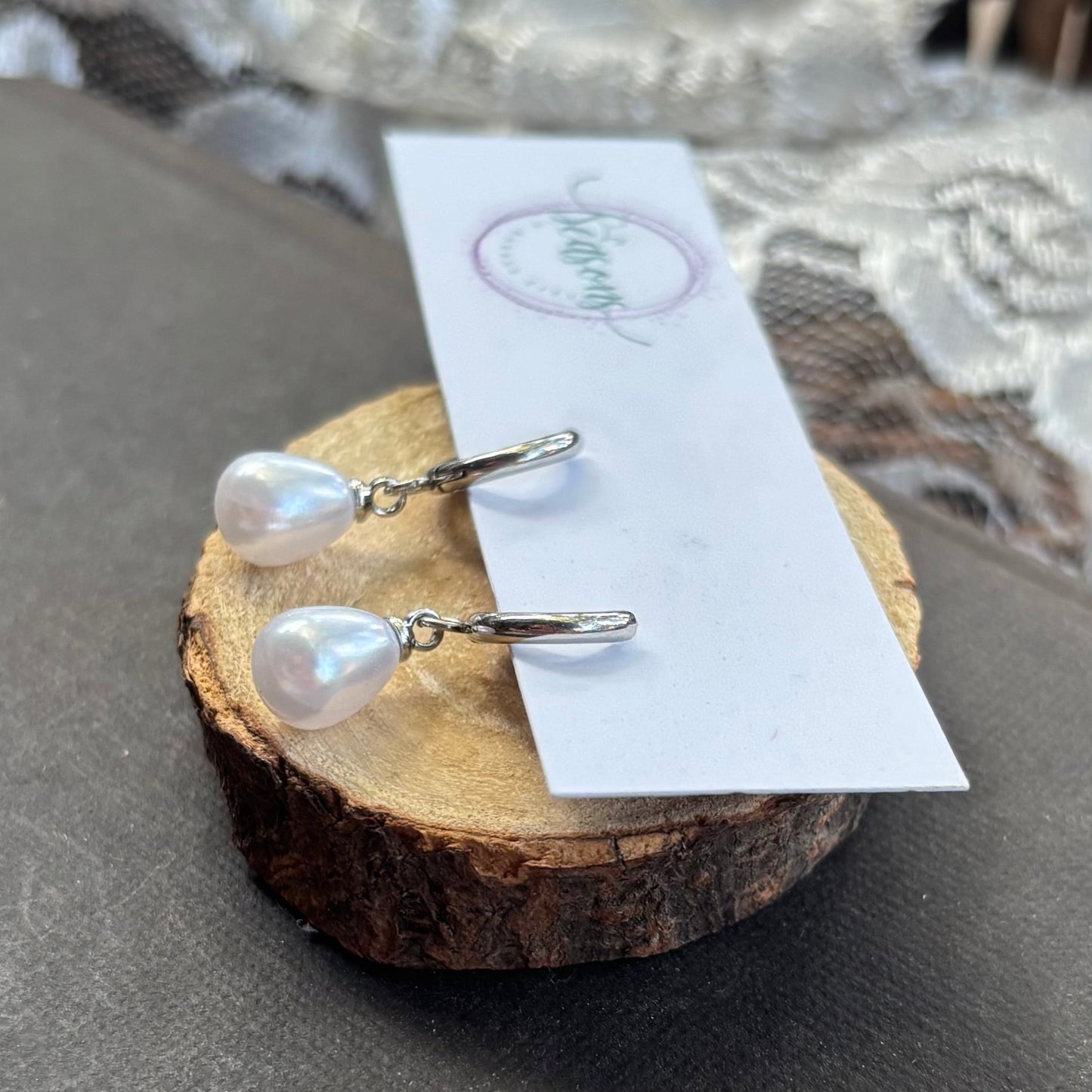 Pair of pearl earrings on a wooden stand with a gray surface and wicker basket in the background.