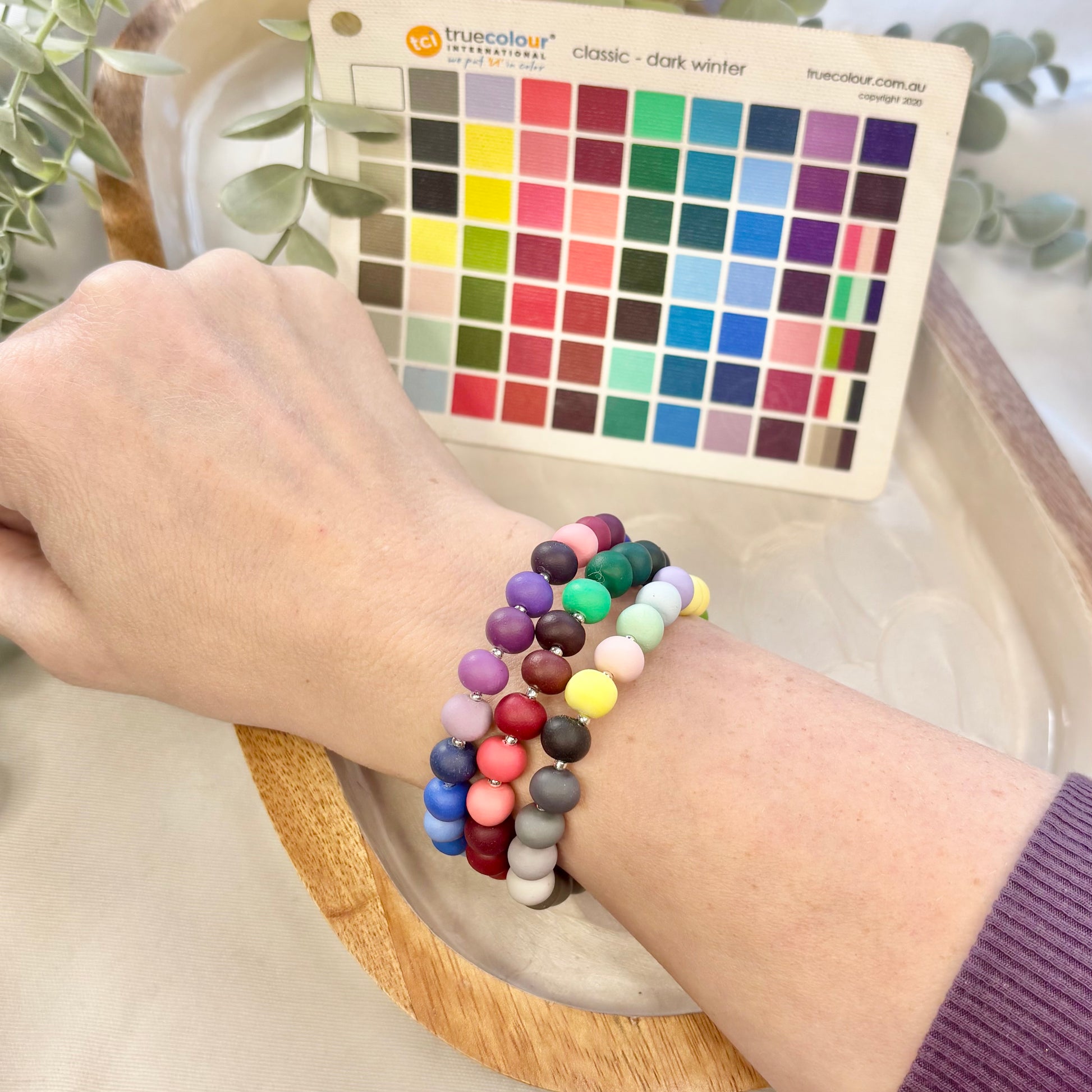 Color swatch card with a hand wearing colorful beaded bracelets on a neutral background